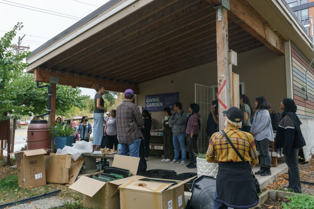 Outside. A group of people ar gathered around a speaker in the UWT giving garden.